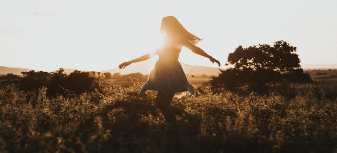 Woman dancing through a field at sunset