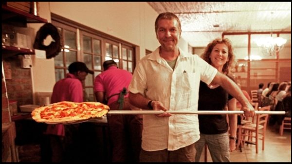 Owner of Massimo's delicately placing a pizza on a pizza peel, ready to be baked in the pizza oven, known for serving the best pizza in Cape Town